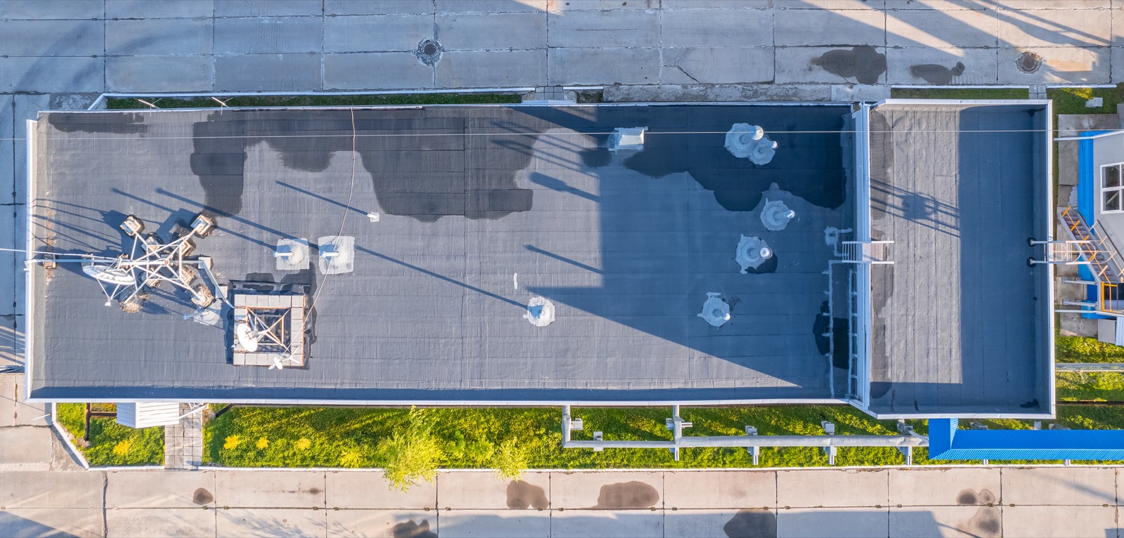 Overhead aerial of a low-slope commercial roof, dark patches of trapped moisture spreading across the membrane
