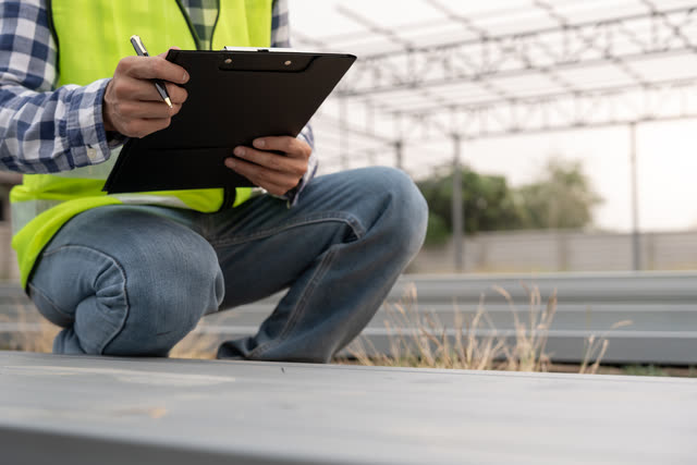 A surveyor in a high-visibility vest making notes on a clipboard